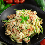 Een bord courgetti (courgettepasta) met tomaat- en feta saus, gegarneerd met een verse basilicumblad, met verse tomaten en courgette op de achtergrond — een koolhydraatarme maaltijd voor gewichtsverlies en een gezond dieet.
