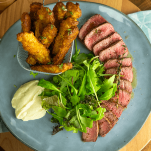 Een bord met plakjes gegrilde biefstuk, knapperige avocadovrijtjes, een frisse groene salade en een romige dipsaus — een heerlijke koolhydraatarme keto maaltijd, ideaal voor gewichtsverlies en een gezond dieet.