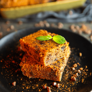 Een stapel van twee vierkante keto blondies met pindakaas, gegarneerd met een muntblaadje en bestrooid met cacaopoeder of kaneel. Een heerlijk koolhydraatarm dessert, perfect voor het keto dieet.