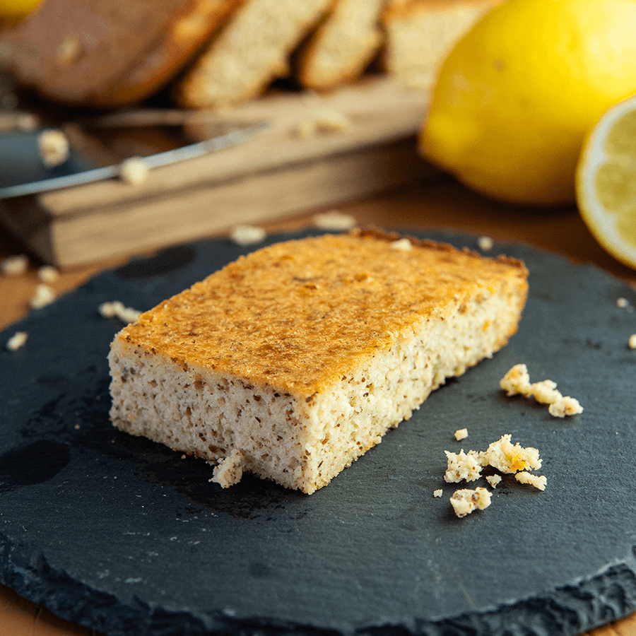 Een plakje keto citroen cake met een vochtige, licht kruimelige textuur, geserveerd op een zwart bord met citroenen op de achtergrond — een koolhydraatarm dessert voor gewichtsverlies en een gezond dieet.