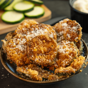 Knapperige keto courgettechips, bestrooid met geraspte Parmezaanse kaas, geserveerd op een blauw bord met een romige dipsaus — een gezonde koolhydraatarme snack voor gewichtsverlies en een gezond dieet