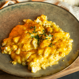 Close-up van een romige keto mac and cheese, gegarneerd met gehakte kruiden en een snufje zwarte peper, geserveerd op een grijs bord — een koolhydraatarme maaltijd ideaal voor gewichtsverlies en een gezond dieet.