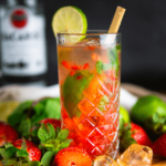 Koolhydraatarme strawberry mojito met rum geserveerd in een hoog glas met ijs, verse aardbeien, muntblaadjes en een limoenpartje. Een verfrissend koolhydraatarm drankje voor gewichtsverlies en een gezond dieet.