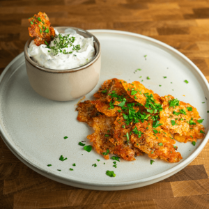 Een bord met knapperige koolhydraatarme Parmezaanse kaaschips geserveerd met een romige kruidendip. Een heerlijke en gezonde snack, ideaal voor gewichtsverlies en het keto dieet.
