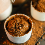 Een Koolhydraatarme brownie met cacao in een wit ramekin, gegarneerd met chocoladestukjes en bestrooid met cacaopoeder. Een snel, eenpersoons dessert voor gewichtsverlies en een gezond dieet.