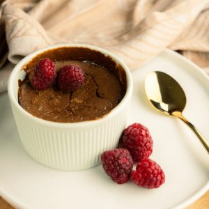 Een romige koolhydraatarme chocolade cheesecake geserveerd in een wit ramekin, gegarneerd met cacaopoeder en verse frambozen — een dessert geschikt voor gewichtsverlies en een gezond dieet
