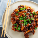 Plate of savory Korean BBQ chicken thigh pieces topped with sesame seeds and fresh garnish