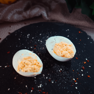 Twee gevulde eieren met romige dooiervulling, bestrooid met paprika en kruiden op een donker gespikkeld bord — een smakelijk keto en koolhydraatarm voorgerecht voor gewichtsverlies en een gezond dieet.