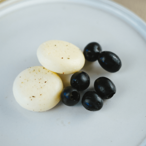 Een klein bord met twee ronde stukjes witte kaas met kruiden en enkele zwarte olijven — een eenvoudige keto snack ideaal voor gewichtsverlies en een gezond dieet
