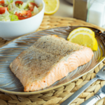 Een perfect gegaarde airfryer zalmfilet gekruid met zwarte peper en geserveerd met citroenpartjes en een frisse salade — een gezonde koolhydraatarme maaltijd voor gewichtsverlies en een gezond dieet