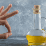 Hand die goedkeurend gebaar maakt naast een fles olijfolie op tafel