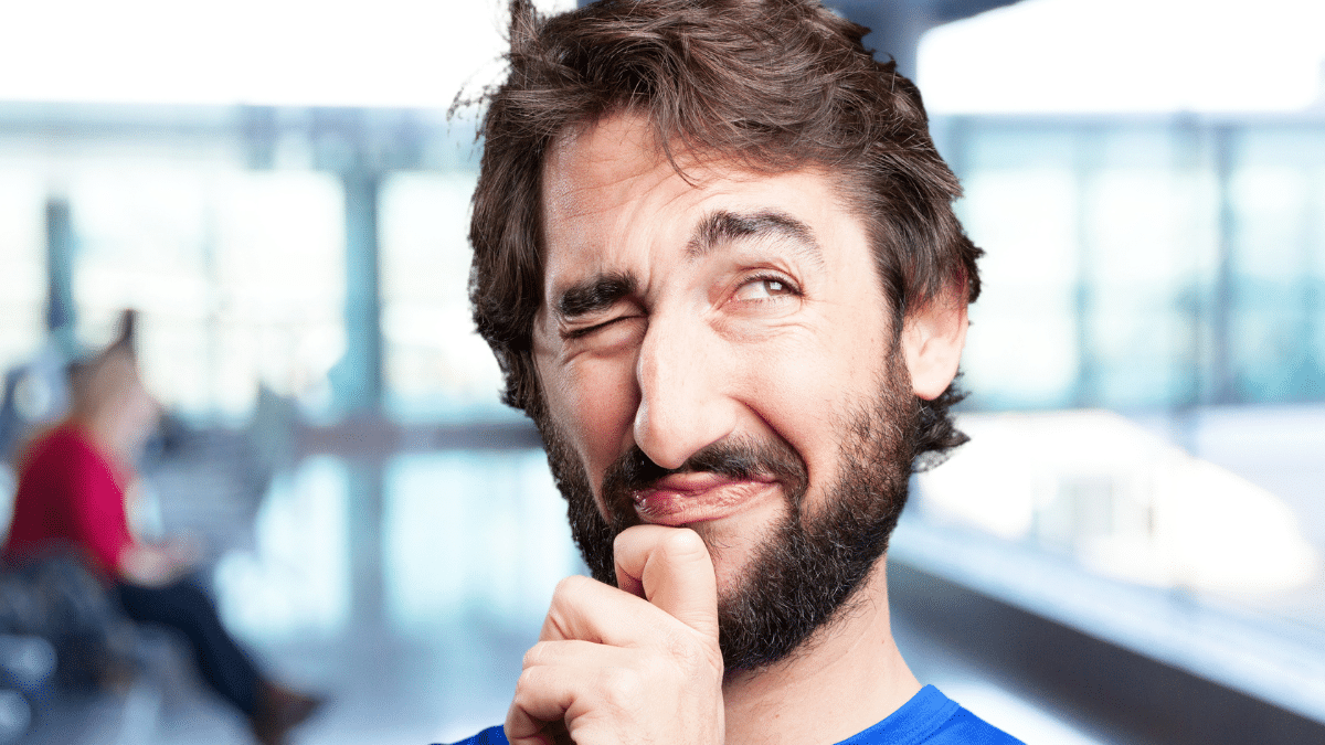 man kijkt bedenkelijk en lacht met opgetrokken wenkbrauw in een lichte binnenruimte