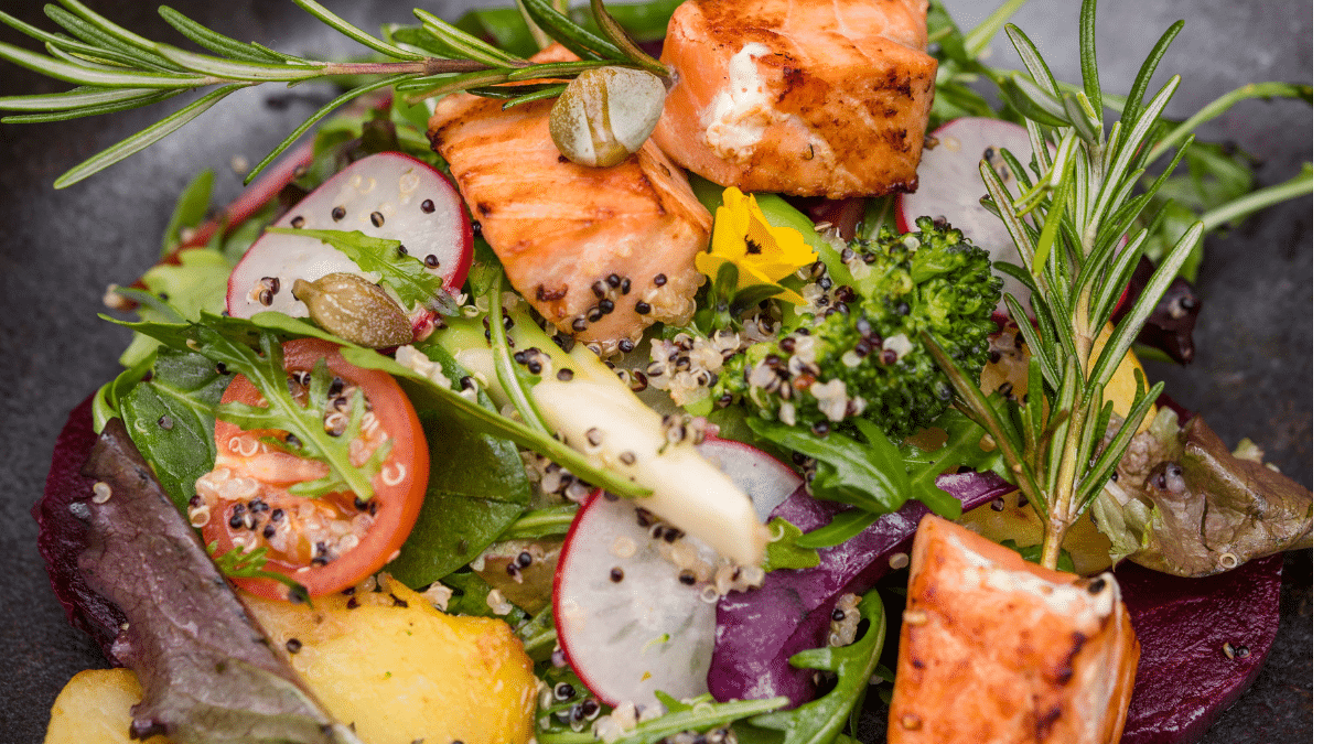 Gezonde maaltijd met zalm, groente en olijfolie op een houten tafel.