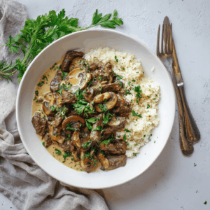 Paleo rundvlees stroganoff met champignons in romige kokosroomsaus geserveerd met bloemkoolrijst en verse peterselie.
