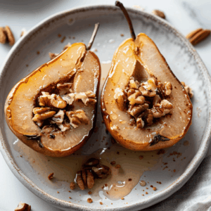 Geroosterde peren met kaneel en noten op een bord, warm gebakken in de oven tot ze zacht en karamellig zijn, gevuld met pecannoten en licht besprenkeld met honing voor een gezonde Paleo dessertoptie.