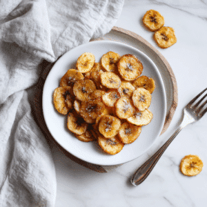 Zelfgemaakte Paleo Bananenchips, goudbruin en knapperig, bestrooid met een beetje zeezout voor een perfecte balans van zoet en zout.