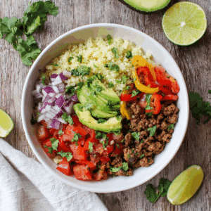 Paleo bloemkoolrijst burrito bowl met gekruid gehakt, avocado, verse tomaat, paprika, rode ui en koriander, een kleurrijke graanvrije en koolhydraatarme maaltijd