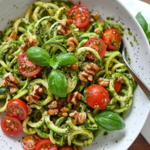 Gezonde paleo courgette-noedels met verse basilicumpesto en kleurrijke cherrytomaten, bereid in een Nederlandse keuken als licht koolhydraatarm gerecht.