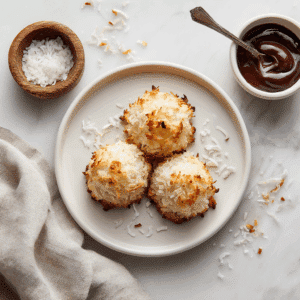 Drie goudbruine kokosmakronen met een lichte, geroosterde textuur aan de bovenkant, bestrooid met geraspte kokos