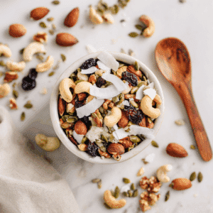 Paleo Trail Mix met noten, zaden, kokosvlokken en gedroogd fruit, waaronder cashewnoten, amandelen, pompoenzaden, zonnebloempitten, en cranberries. De mix is versierd met kokosvlokken en biedt een voedzame, knapperige snack, perfect voor onderweg.