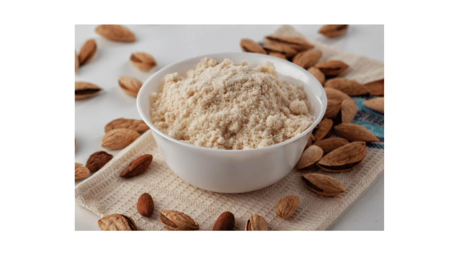 Close up van een kom gevuld met amandelmeel, omringd door hele amandelen. De afbeelding benadrukt de rol van amandelmeel als een veelgebruikt en natuurlijk ingrediënt binnen paleo bakken.