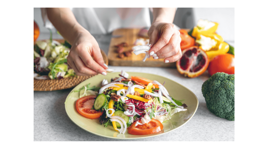 Een kleurrijke schaal met verse groenten zoals tomaat, komkommer, paprika en ui die wordt bereid in een gezonde keukenomgeving. De afbeelding laat zien hoe pure voeding en verse ingrediënten centraal staan in een paleo vriendelijke maaltijd.