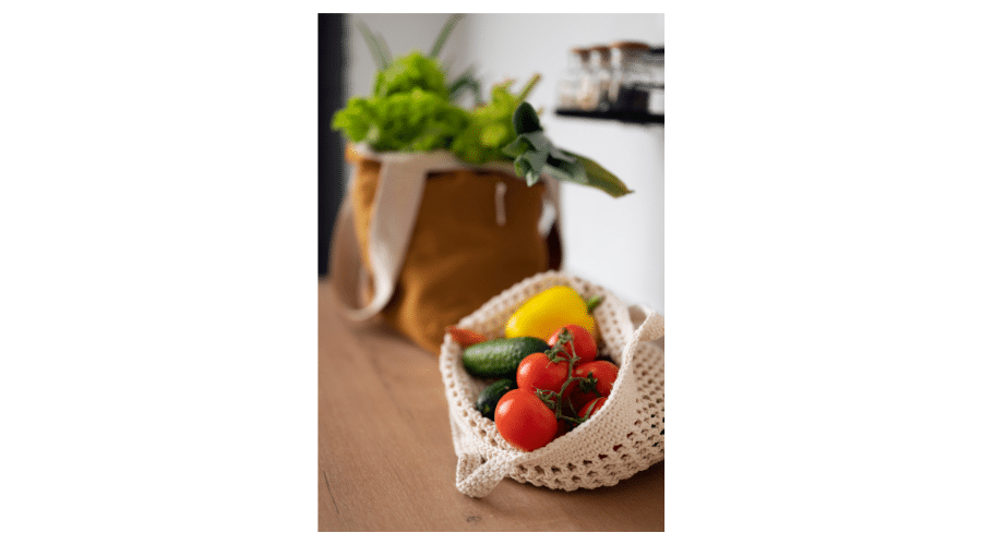 Verse paleo vriendelijke boodschappen met onder andere tomaten komkommer paprika en bladgroenten in herbruikbare tassen. De afbeelding laat zien hoe gezonde en natuurlijke ingrediënten de basis vormen voor een pure en overzichtelijke keuken.