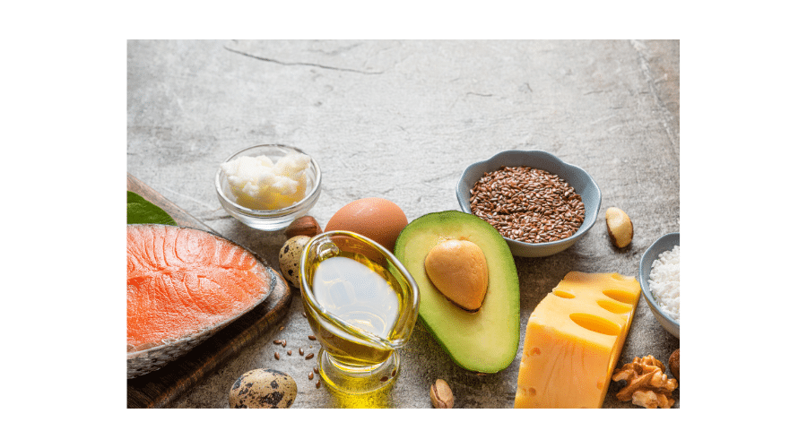 Een selectie van gezonde vetten zoals zalm, avocado, olijfolie, eieren, zaden, noten en kaas op een stenen ondergrond. De afbeelding laat zien hoe natuurlijke vetrijke producten bijdragen aan een voedzame en paleo vriendelijke leefstijl.