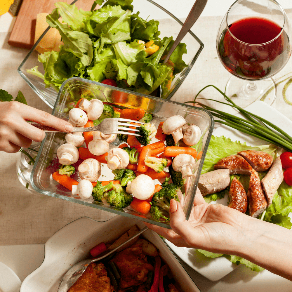 Bord met een gezonde koolhydraatarme maaltijd van gegrilde kipworst, verse groenten en een salade met een glas rode wijn op tafel.
