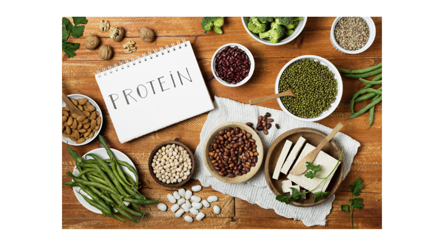 Een overzicht van eiwitrijke voedingsmiddelen zoals bonen, noten, tofu en groenten op een houten tafel, met een notitieblok waarop het woord protein staat. De afbeelding laat zien hoe verschillende natuurlijke eiwitbronnen bijdragen aan een gezonde en voedzame leefstijl.