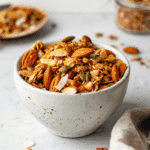 Paleo Granola Clusters met amandelen, pompoenpitten, zonnebloempitten, kokosvlokken en andere noten. De granola is goudbruin, knapperig en vol van textuur, ideaal als gezonde snack of ontbijt.