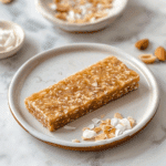 Paleo Zelfgemaakte Kokos Energie Repen, gemaakt van kokos, noten en dadels, met een zachte, taaie textuur en omringd door geschaafde kokosvlokken en amandelen. Perfect voor een gezonde snack of energieboost.