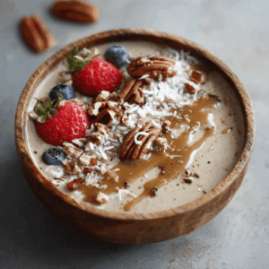 Keto pecan vanille smoothie bowl in een houten kom, romige koolhydraatarme smoothie gegarneerd met aardbeien blauwe bessen pecannoten geraspte kokos en notenboter, gezond keto ontbijt met zachte textuur gefotografeerd van bovenaf in natuurlijk licht