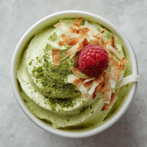 Keto kokos matcha mousse – romige, koolhydraatarme dessertmousse van kokosroom en amandelboter, getopt met geroosterde kokosvlokken, verse frambozen en matchapoeder, ideaal voor gezonde keto-eters en low-carb liefhebbers.