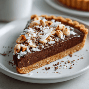 Vegan Keto Chocolade Macadamia Taart – kleine koolhydraatarme desserttaart met romige kokosroom, amandelpasta en gehakte macadamianoten, op een krokante amandel- en kokosbodem, ideaal als gezond keto-dessert of suikervrije traktatie.