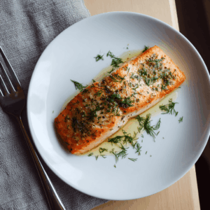 Een perfect gegaarde zalmfilet uit de airfryer, licht goudbruin aan de buitenkant en zacht van binnen, afgewerkt met verse dille en een vleugje citroen. Het gerecht oogt fris, romig en aromatisch op een eenvoudig bord.