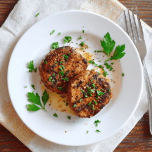 Twee goudbruine varkenshaasmedaillons uit de airfryer, licht gekruid met paprika, peper en knoflook, met een sappige en malse structuur. Het gerecht is geserveerd op een bord en afgewerkt met een vleugje fijngehakte peterselie.