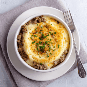 Keto airfryer gehakt ovenschotel met romige bloemkoolpuree en gesmolten kaas, goudbruin gebakken in een ovenschaaltje en afgewerkt met bieslook.