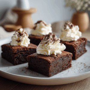 Een klein ovenschaaltje met vier versgebakken keto chocolade brownies uit de airfryer. De brownies hebben een diepe, donkere chocoladekleur met een licht knapperige bovenkant en een zachte, smeuïge binnenkant. Ze zijn netjes in vier stukjes verdeeld en worden warm geserveerd, eventueel met een toef slagroom ernaast. De setting straalt een huiselijke, rijke en uitnodigende chocoladetraktatie uit.